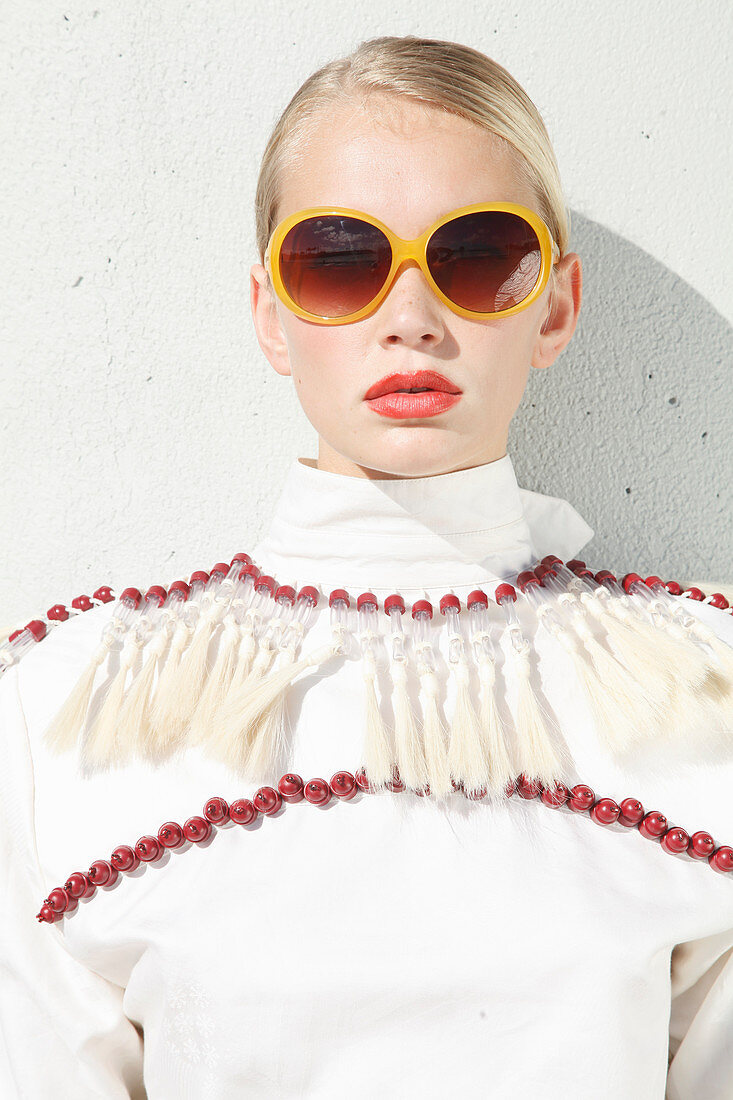 Junge blonde Frau mit Sonnenbrille in weißer Bluse mit roten Perlen