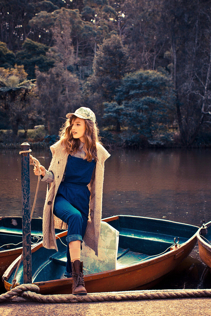 A young woman wearing a blue jumpsuit and a sand-coloured poncho in a boat