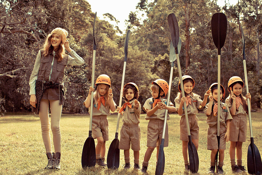 Junge Frau mit Kindern in Uniform mit Paddeln auf der Wiese stehend
