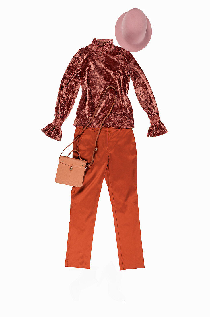 A ruffled velvet blouse and suit trousers in shiny copper tones with a hat and a shoulder bag
