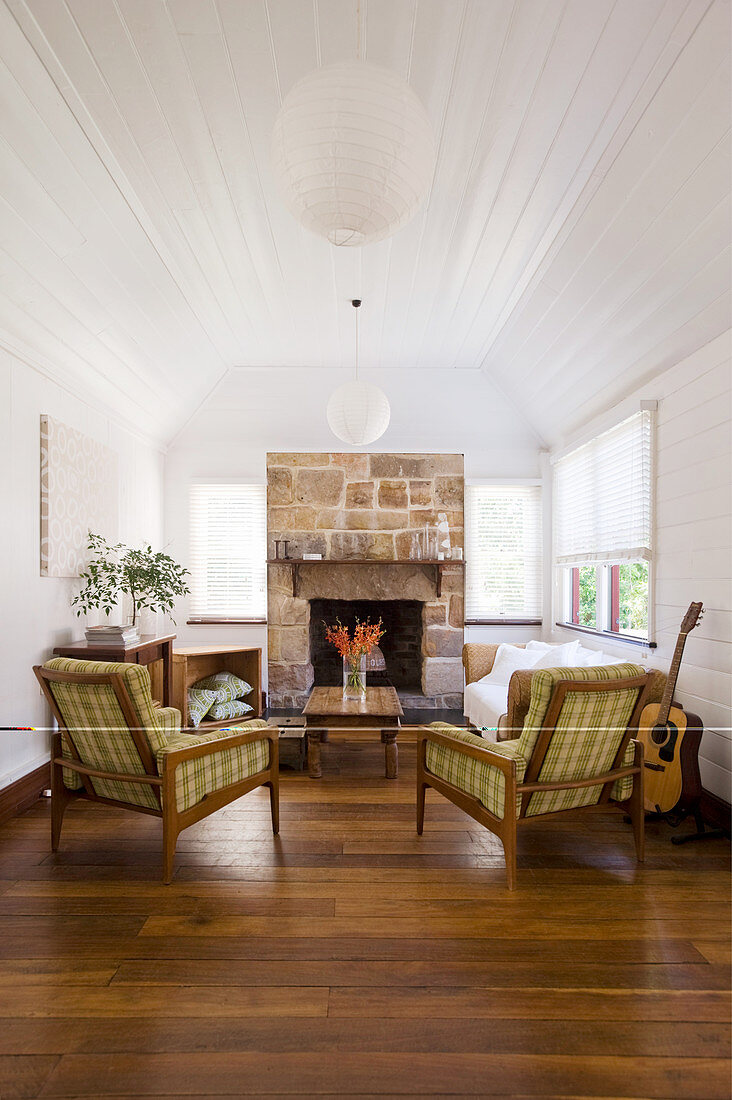 Armchairs with tartan covers, couch and coffee table in front of fireplace in living room with white-painted wood-clad walls