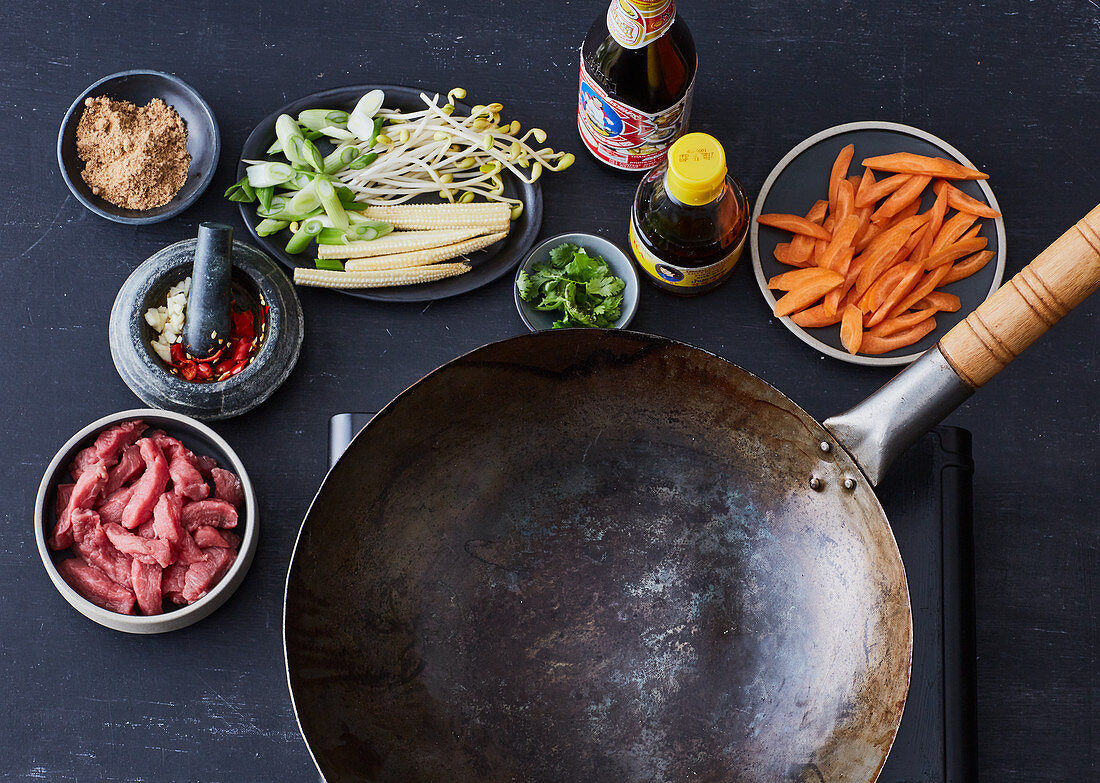 A stir-fry arrangement - a wok, meat, carrots, coriander and chilli