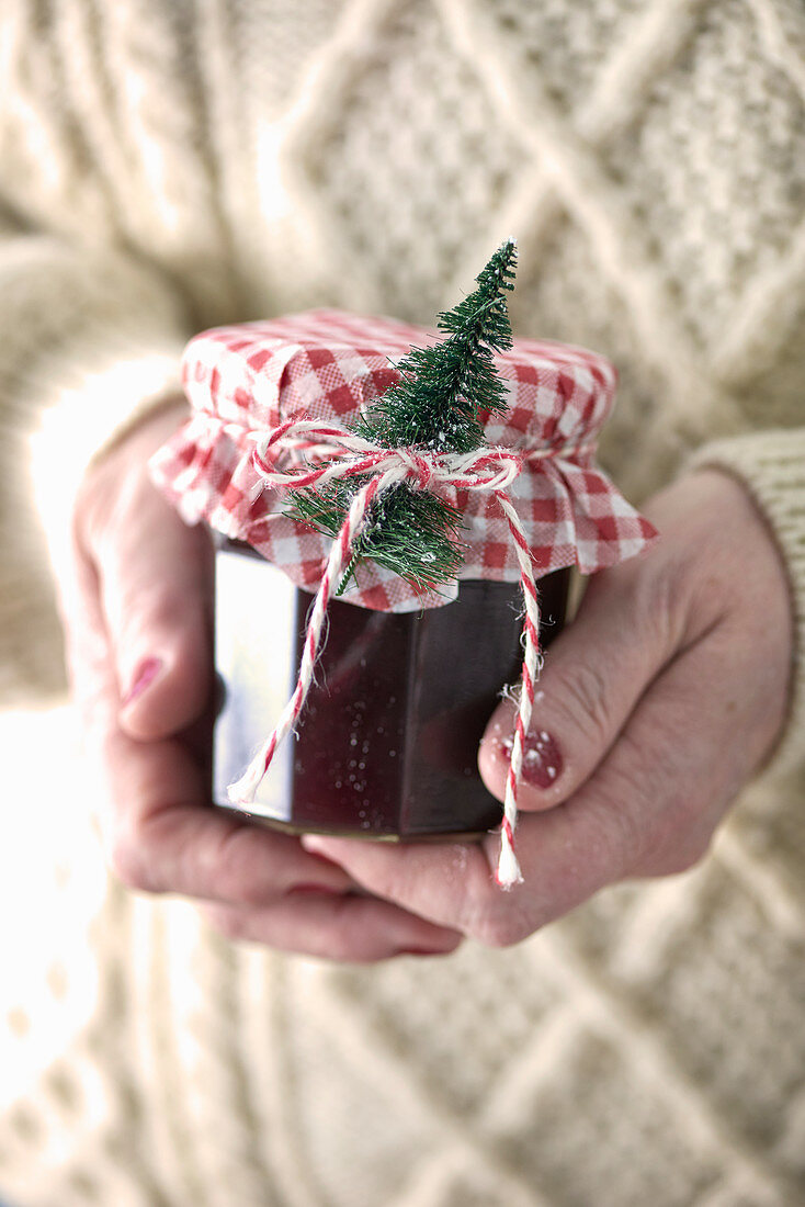 Hand hält weihnachtlich dekoriertes Marmeladenglas