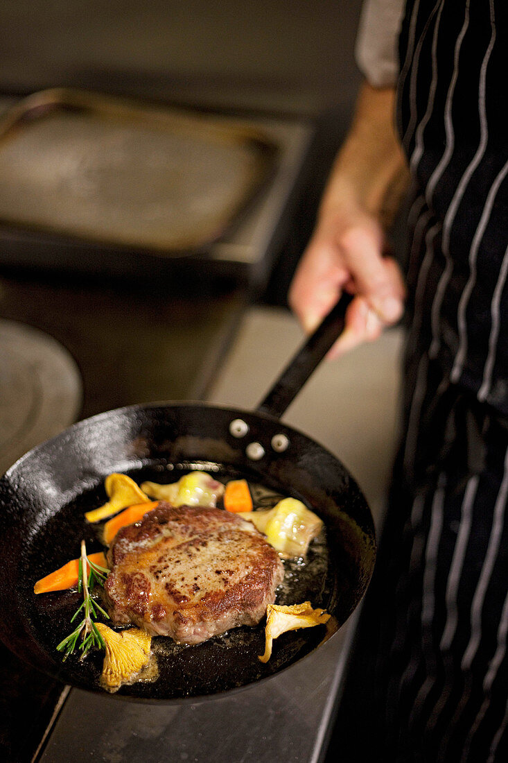 Rib eyed steak with chanterelle mushrooms and vegetables in a pan held by a chef