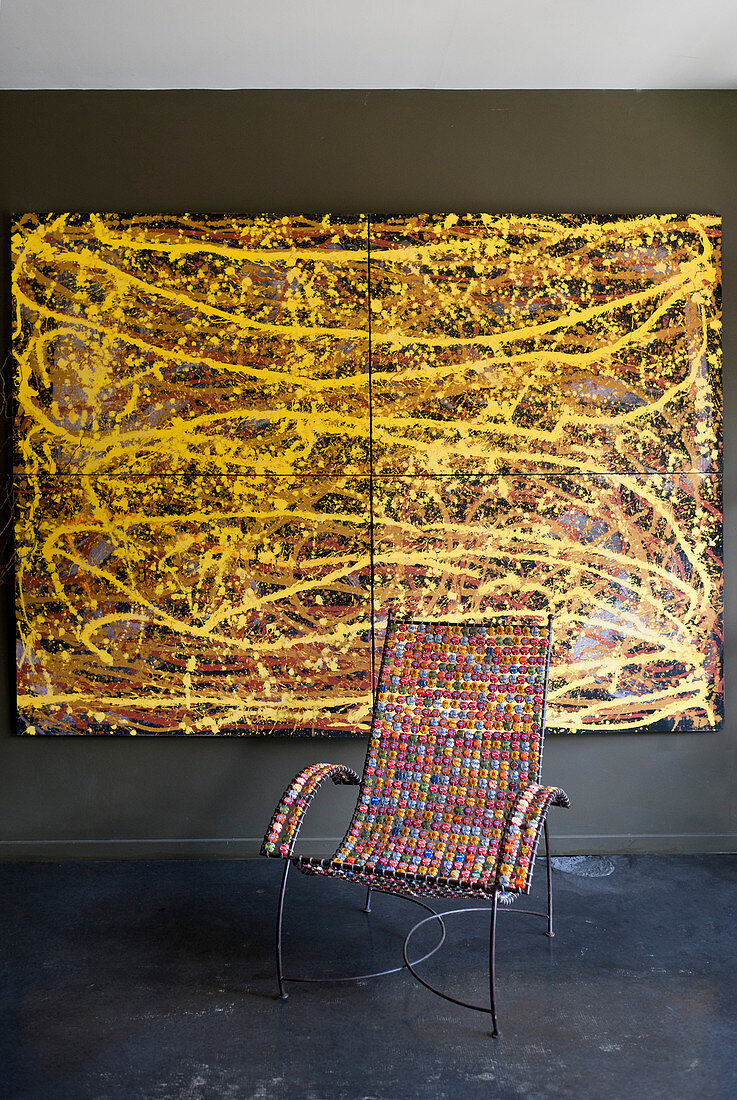 Metal chair with colourful beaded seat and arms in front of painting