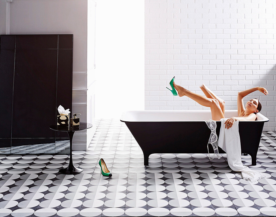 Schwarz-weißes Badezimmer mit Zementfliesen, Frau in der Badewanne