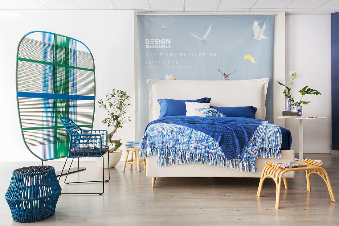 Bettwäsche in Blautönen auf weißem Doppelbett mit Bettkopfteil in offenem Schlafraum mit Raumteiler
