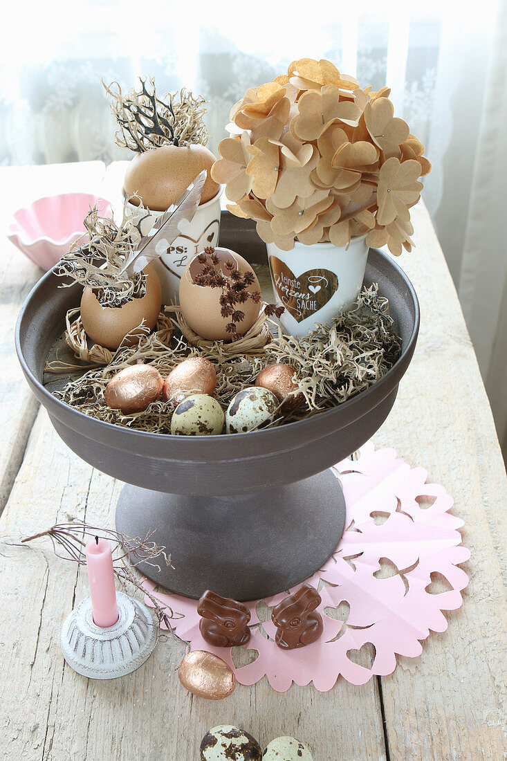 Various Easter eggs and quail eggs on cake stand and chocolate bunnies on table