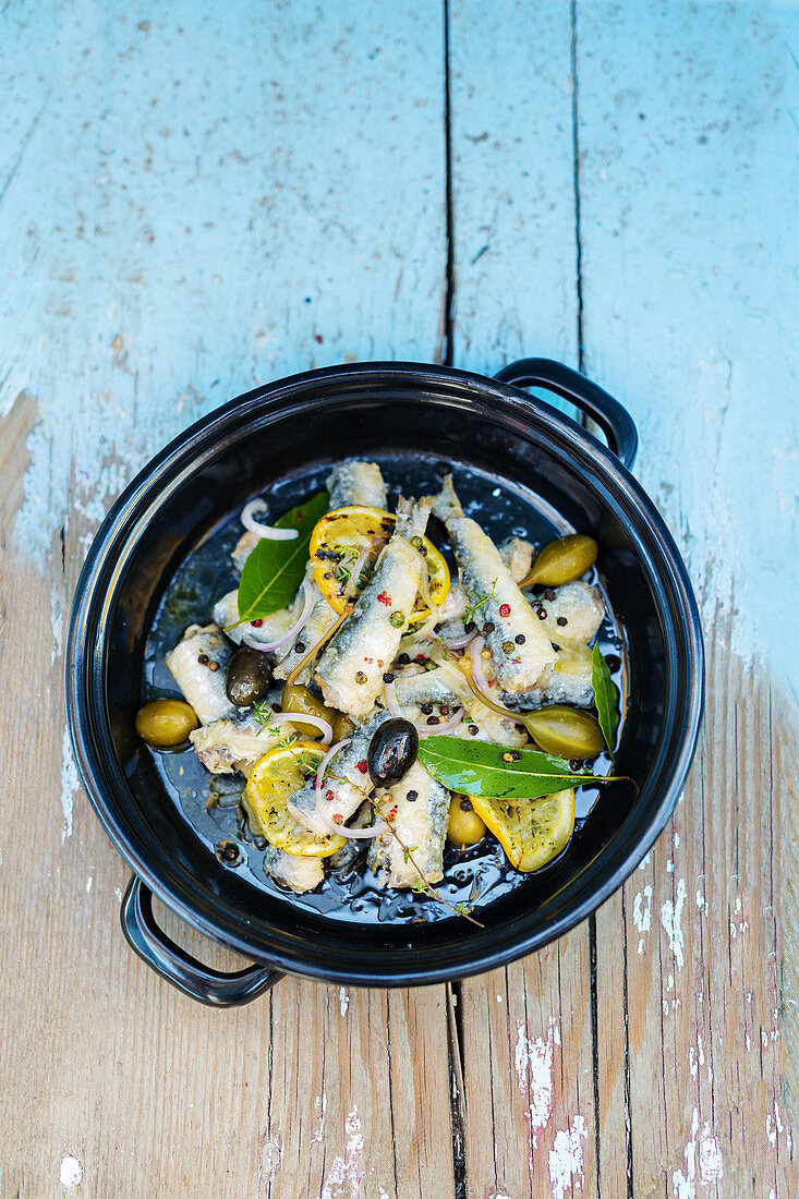 Marinated fish with olives, lemons and spices in a bowl (top view)