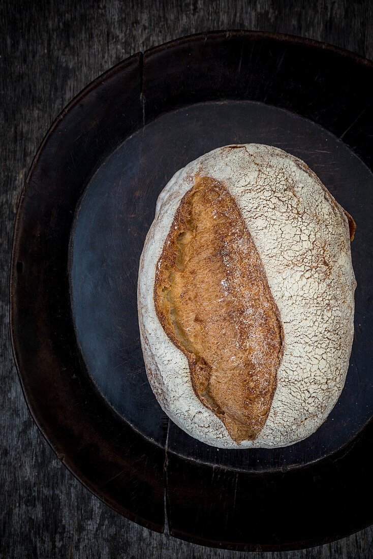 Ein Sauerteigbrot auf schwarzem Teller (Aufsicht)