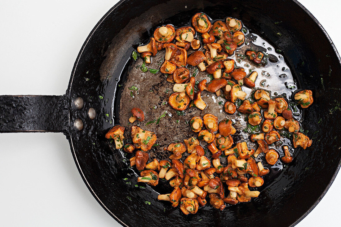 Wild mixed mushrooms frying in a pan with butter and herbs