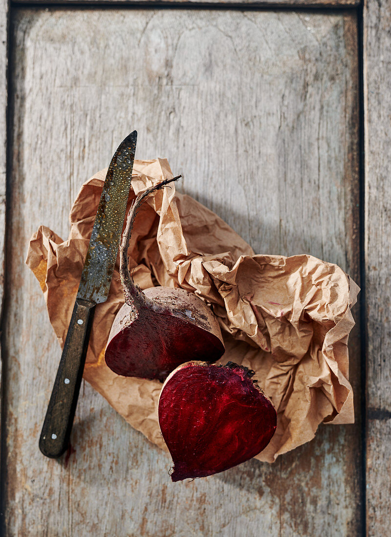 Halved beetroot on a board with brown paper and a knife