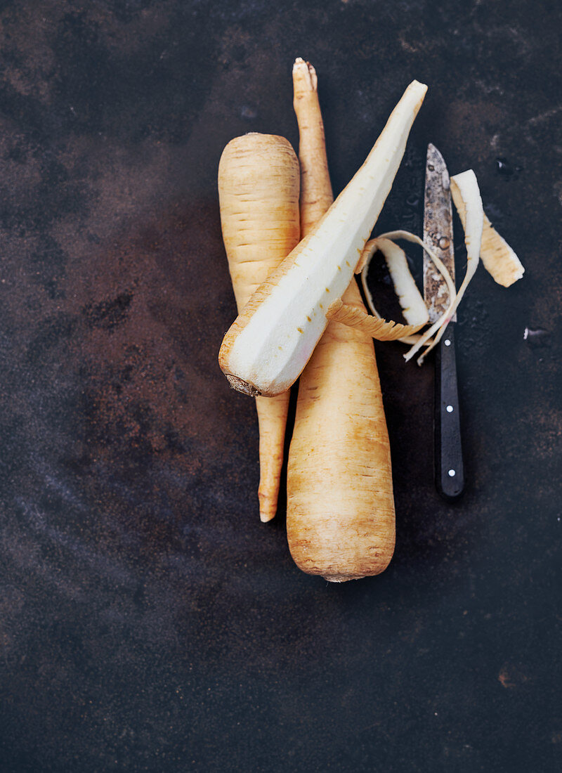 Parsnips, whole and peeled, with a knife