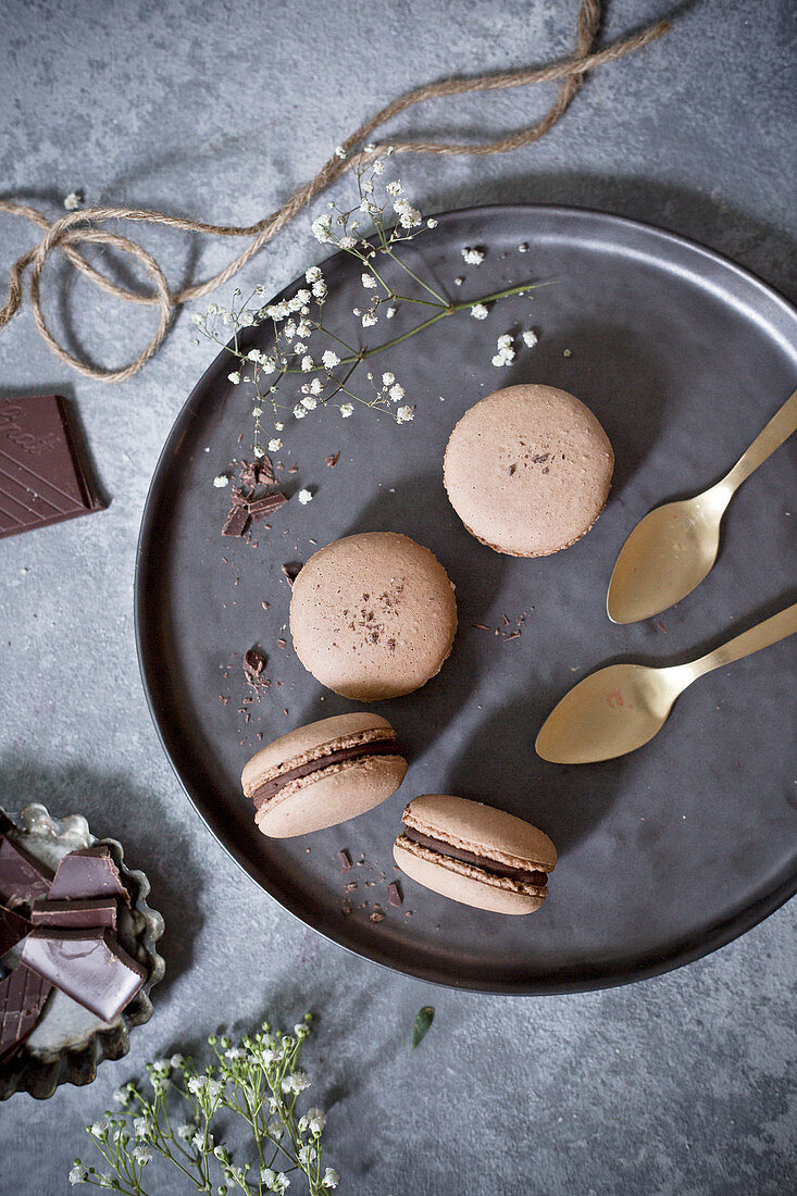 Chocolate macarons with golden spoons on a serving plate (top view)