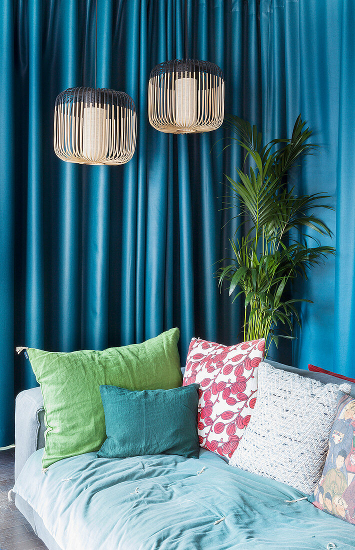 Various scatter cushions on sofa in front of petrol-blue curtain