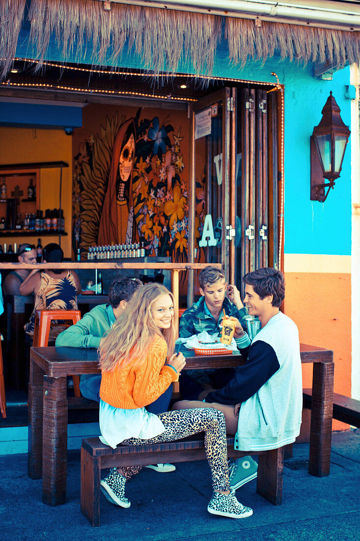 A group of young people wearing fashionable clothing sitting on a terrace at a restaurant