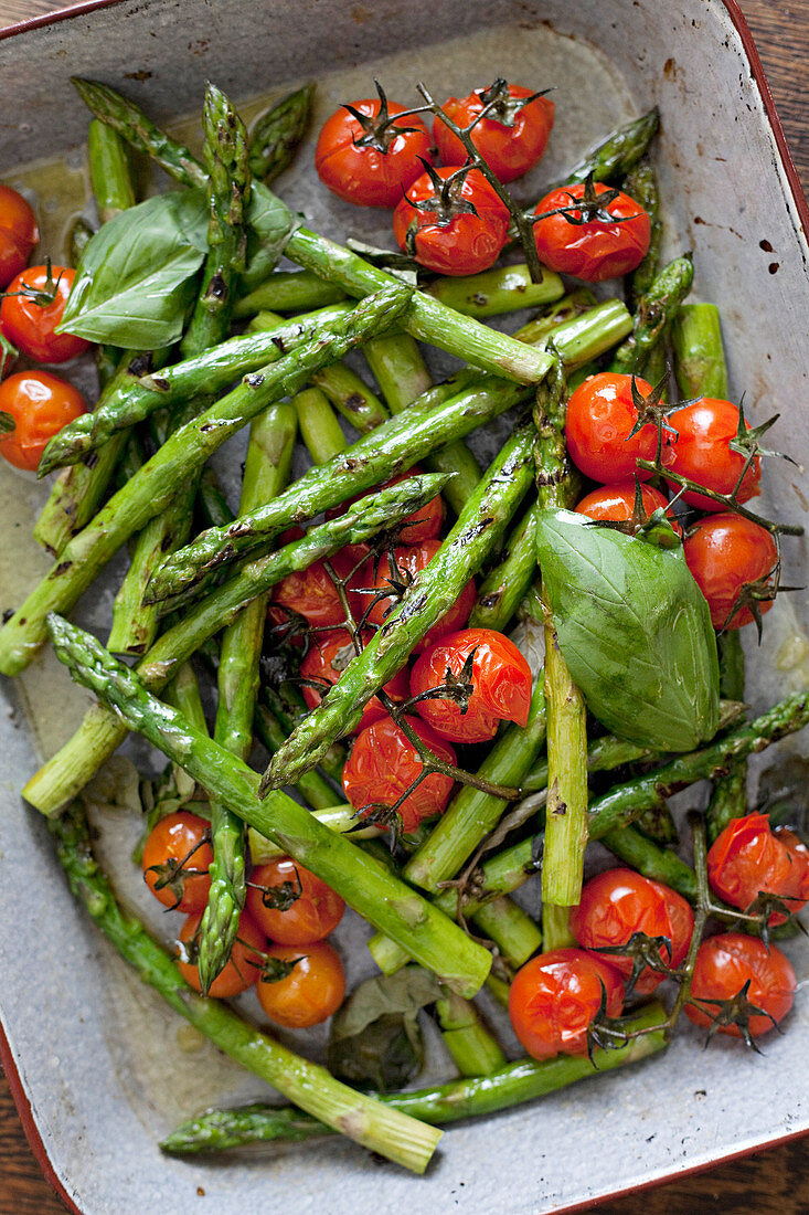 Asparagus and tomatoes topped with basil in a roasting tray almost filling the frame