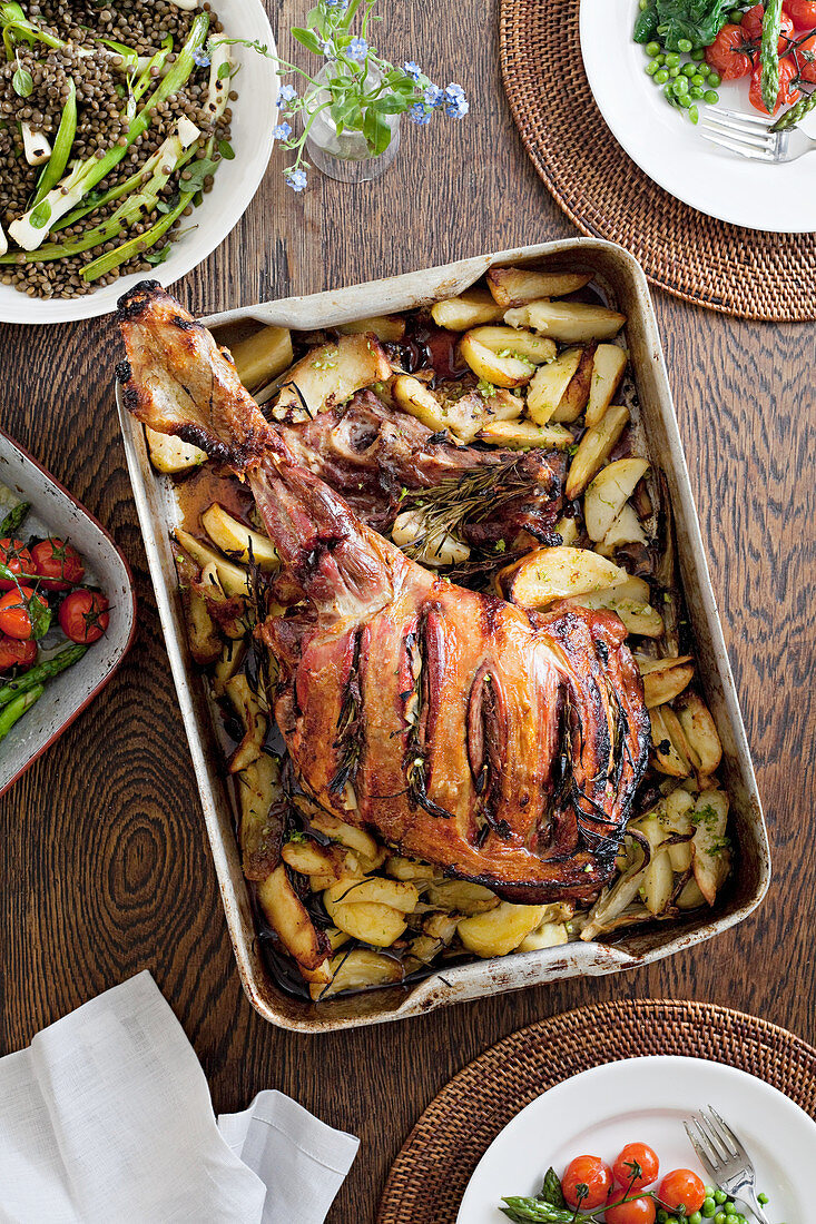 Roasted leg of lamb in a baking tray on the table along with other vegetable dishes