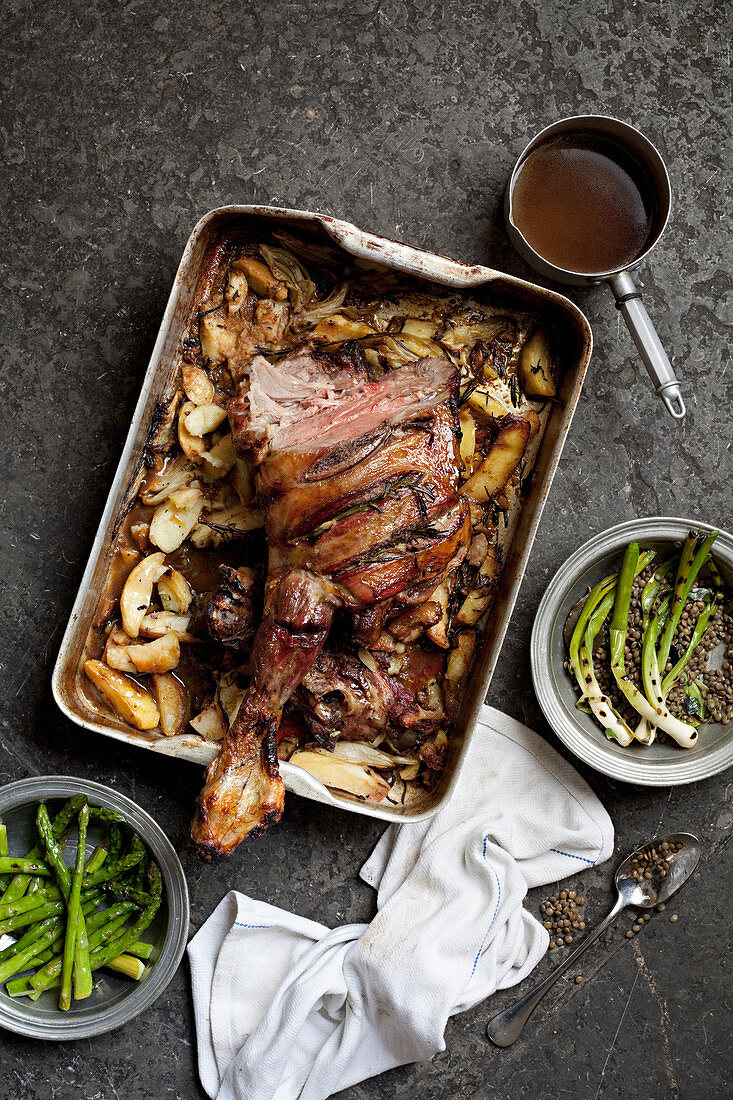 Roasted leg of lamb in a baking tray on the table along with gravy and other vegetable dishes