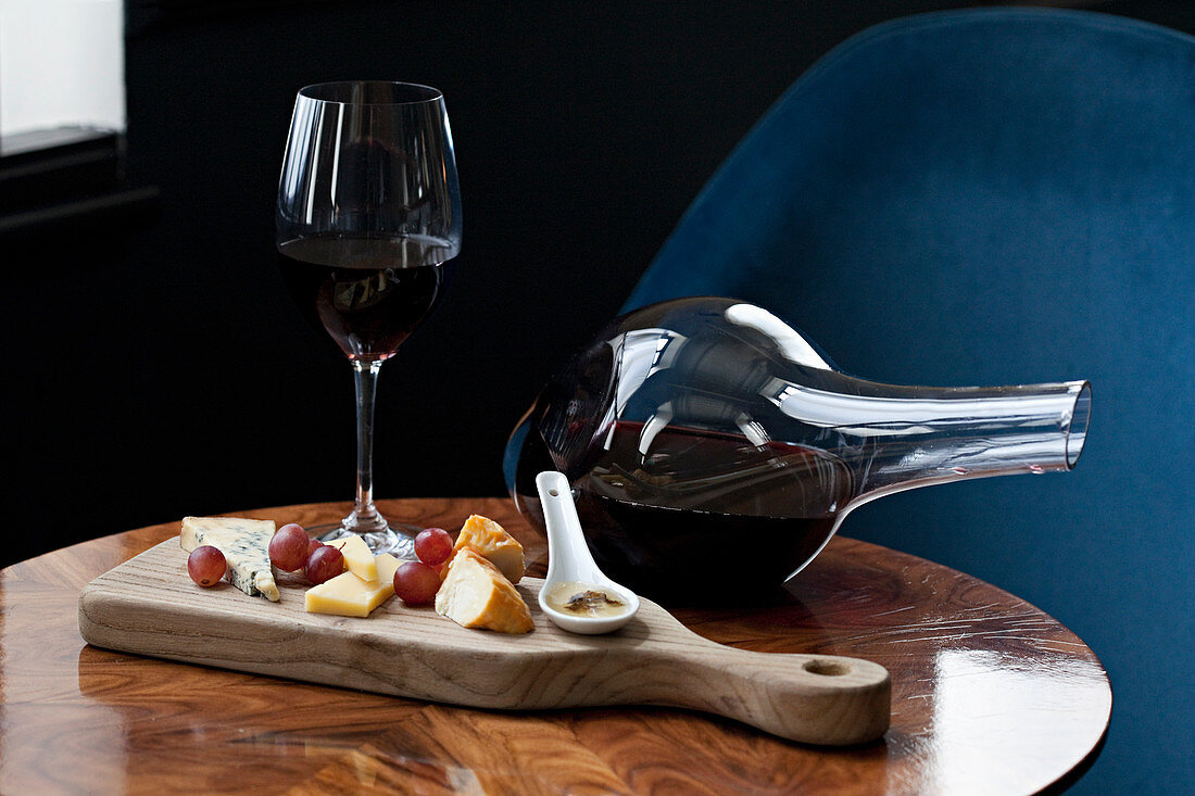 Cheese board on a table with a glass of red and a wine decanter