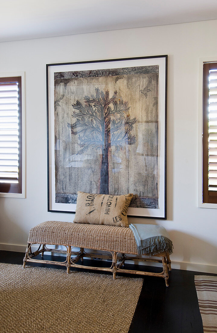 Rattan bench with cushion made from old sack below picture of tree