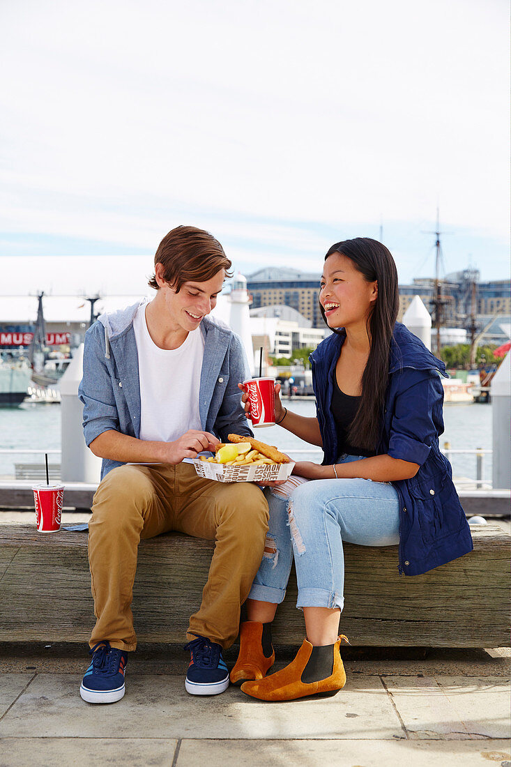 A young couple sitting on a bench sharing fast food