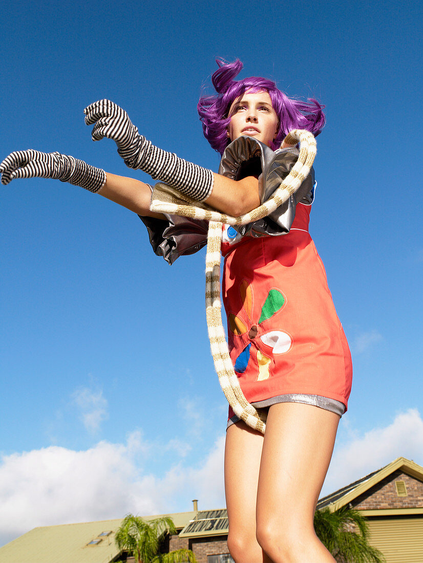 A young woman with purple hair wearing a colourful, futuristic dress with gloves