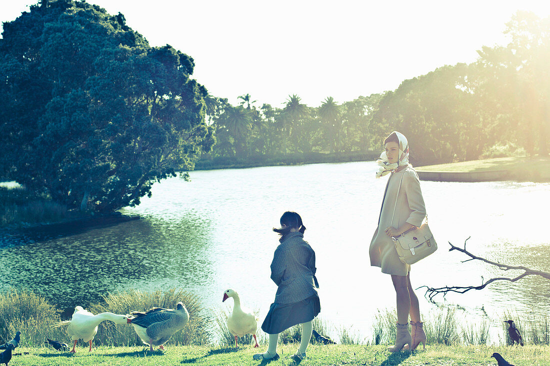 A young woman sitting with a little girl by a lake with birds