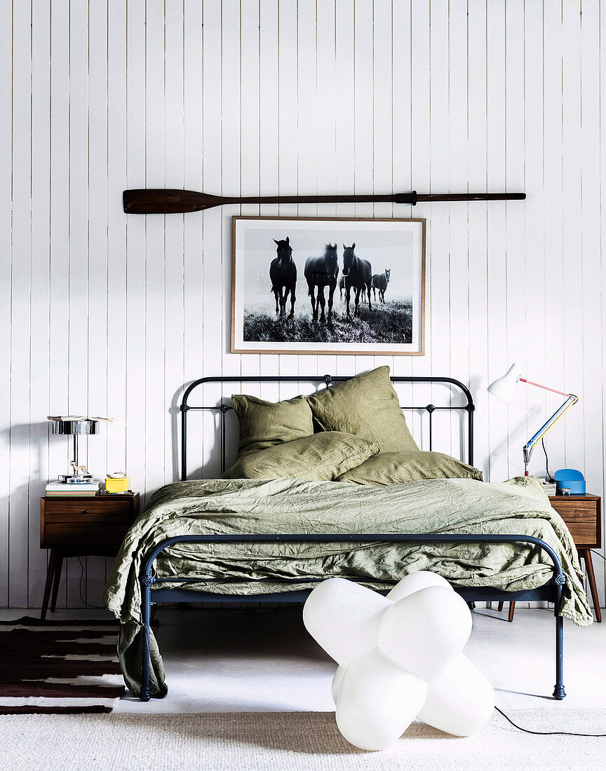 Metal bed with green bedding, above picture with horse motif and paddle