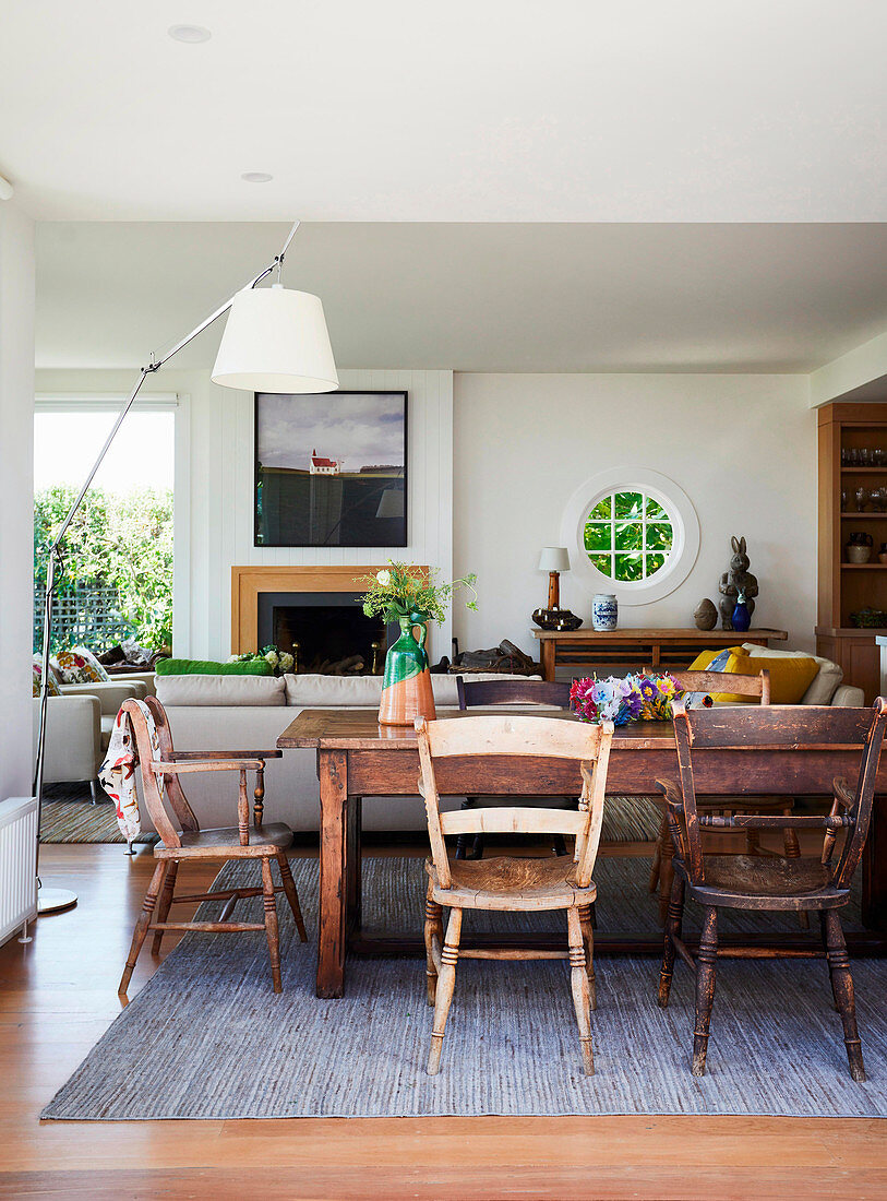 Dining table with rustic wooden chairs, in the background a seating area with a modern fireplace