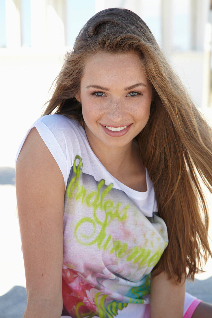 A young blonde woman on a beach wearing a colourful t-shirt