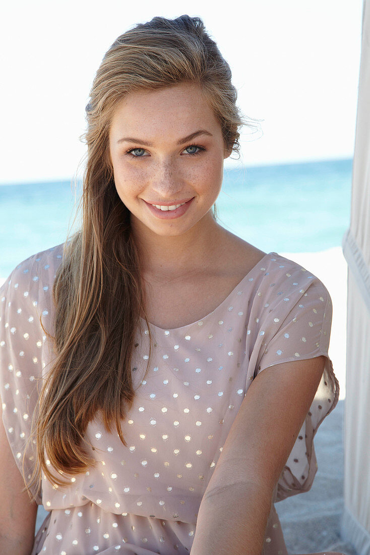 Junge blonde Frau in beigem Pünktchenkleid am Strand