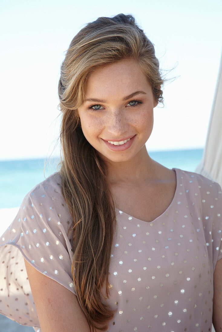 A young blonde woman on a beach wearing a beige polka-dot dress