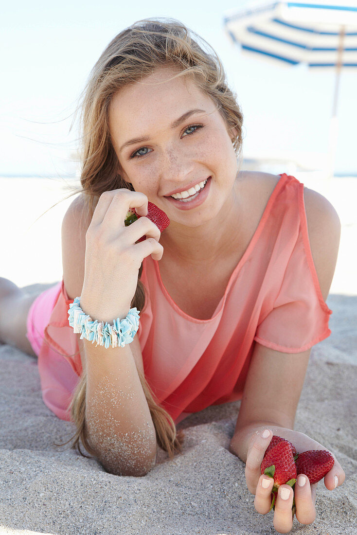 A young blonde woman on a beach wearing a salmon-coloured, off-the-shoulder top