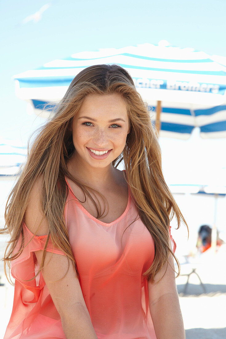 A young blonde woman on a beach wearing a salmon-coloured, off-the-shoulder top