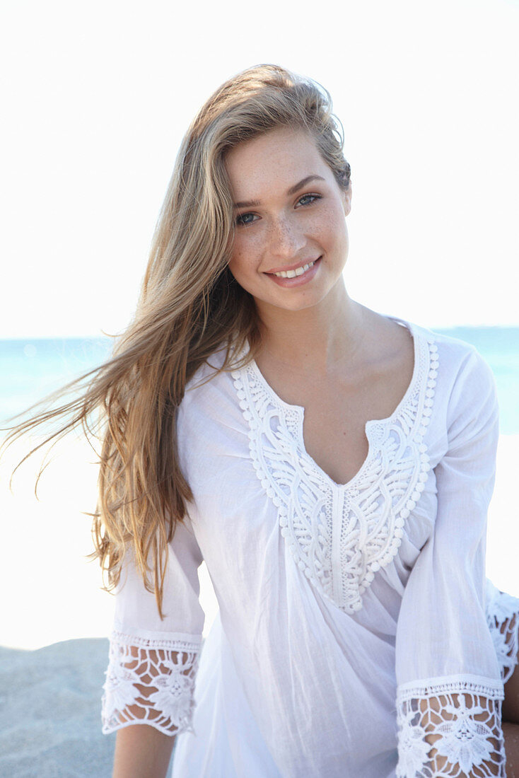 A young blonde woman on a beach wearing a white summer dress