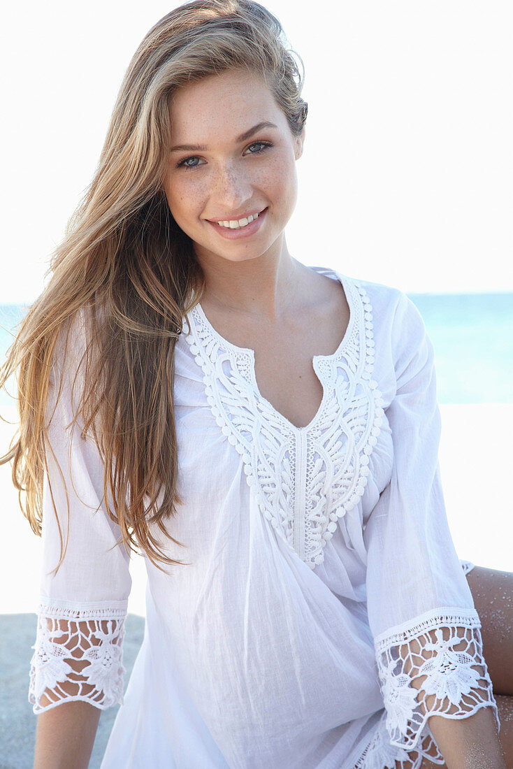 A young blonde woman on a beach wearing a white summer dress