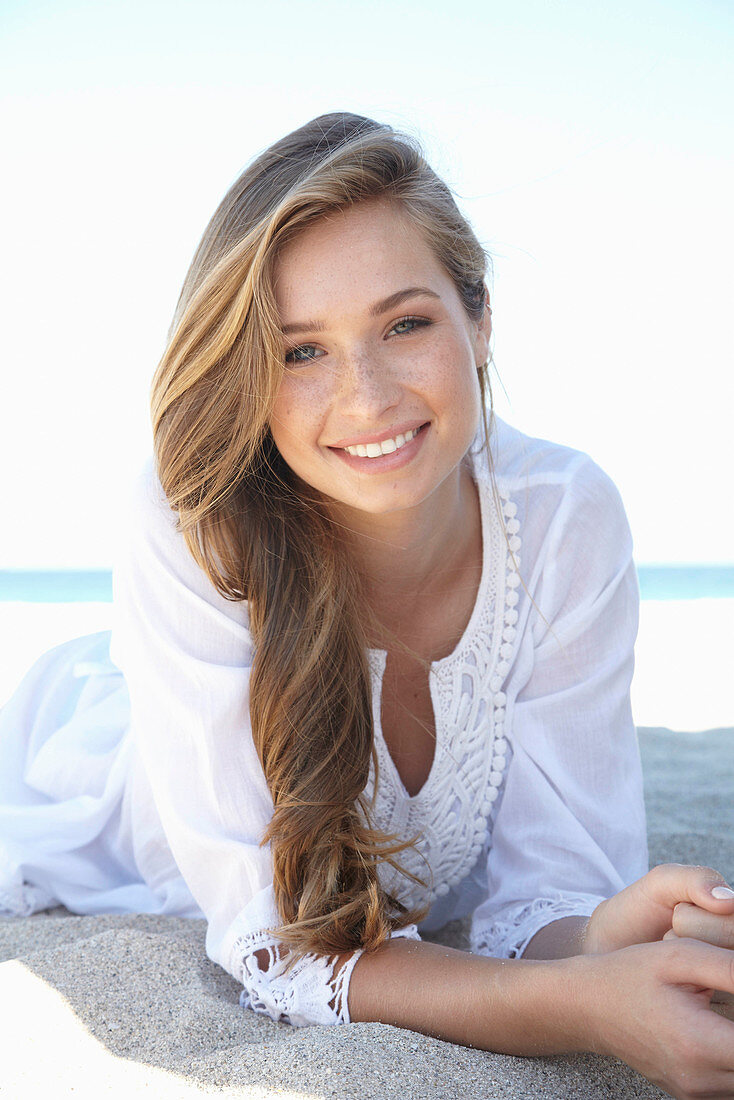 A young blonde woman on a beach wearing a white summer dress