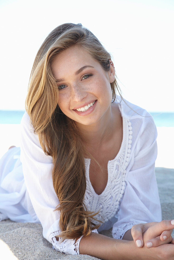 A young blonde woman on a beach wearing a white summer dress