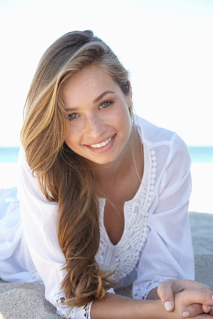 A young blonde woman on a beach wearing a white summer dress