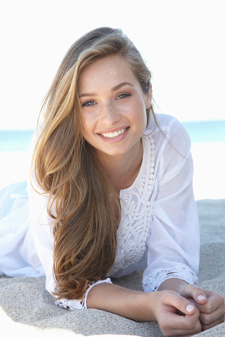 A young blonde woman on a beach wearing a white summer dress