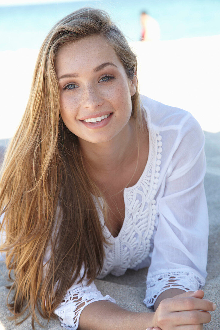 A young blonde woman on a beach wearing a white summer dress