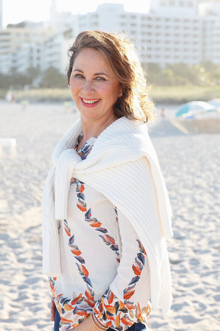 A brunette woman wearing a printed tunic and a white knitted jumper