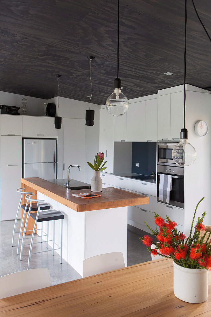 Bar stool on kitchen island with wooden worktop, white fitted kitchen in open living room