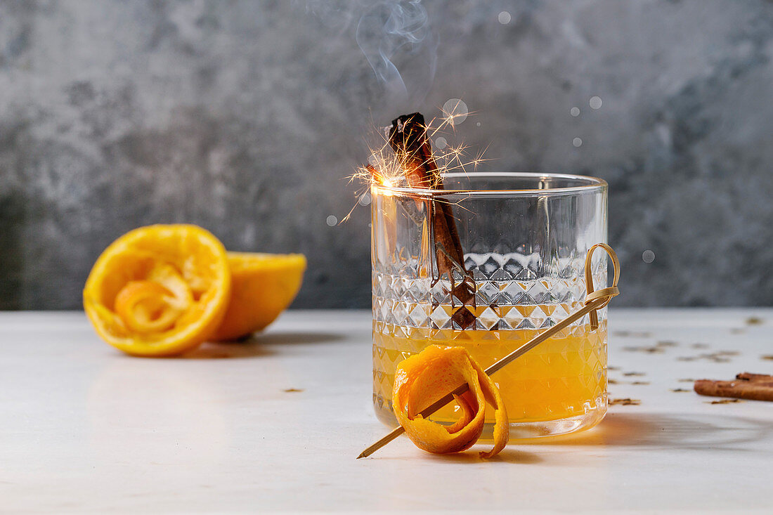 Glass of Scotch Whiskey orange juice alcohol cocktail with swirled orange peel and smoking cinnamon sticks