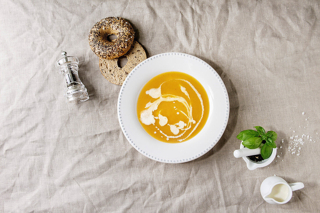 Plate of vegetarian pumpkin carrot soup decorated by cream served with herbs