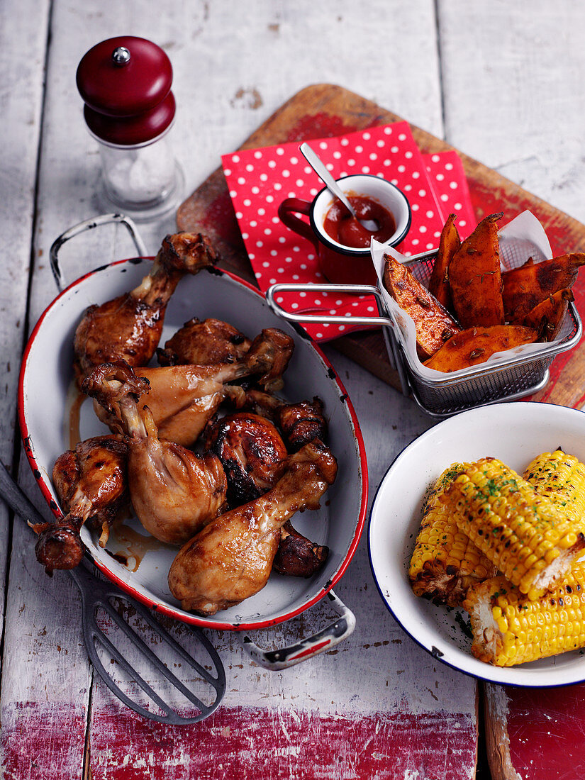 Grilled chicken drumsticks, corn on the cob and sweet potato wedges