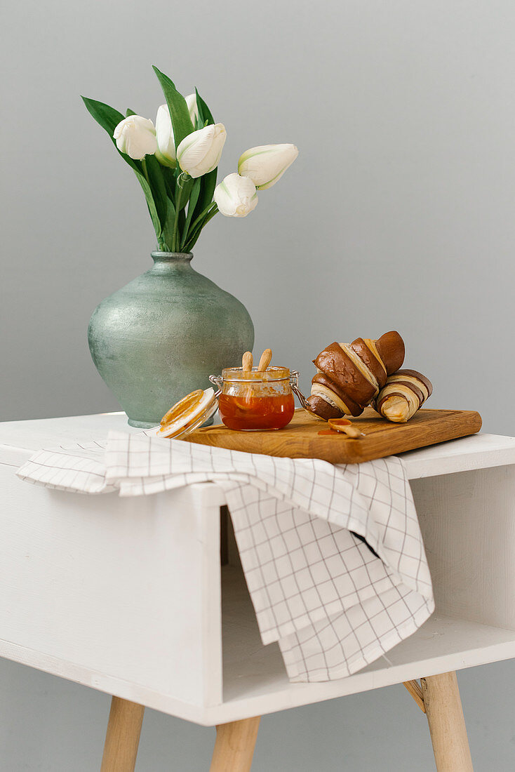 Frühstückshörnchen mit Marmelade neben Blumenvase mit Tulpen auf Tischchen