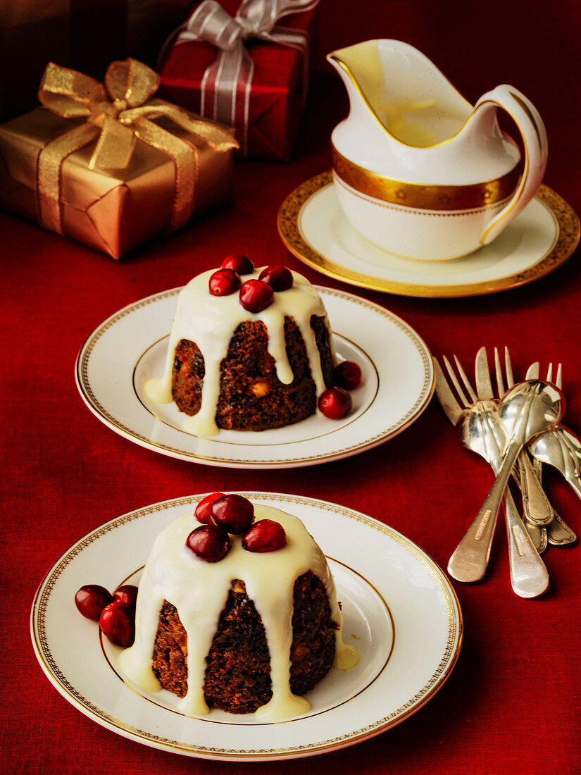 Kleine englische Christmas Puddings serviert mit Rumsauce und Cranberries