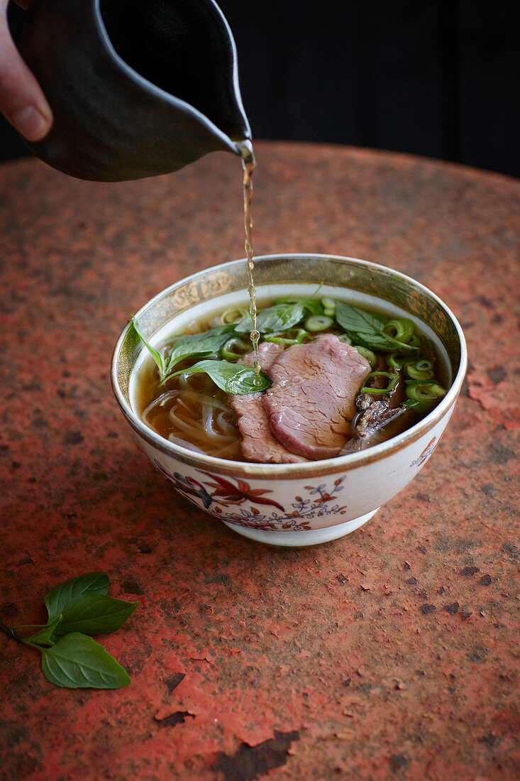 Beef broth being added to Vietnamese pho